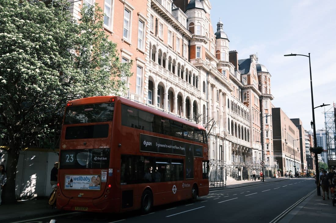 Red London double-decker bus passing a row of Victorian red-brick buildings on a sunny day